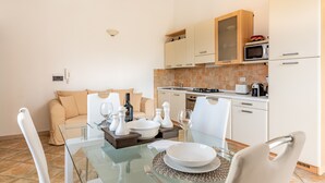 Une cuisine moderne avec des meubles blancs, un four à micro-ondes et un coin repas comprenant une table et des chaises en verre.