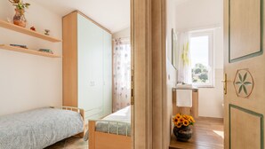 Une chambre à coucher comprenant un lit, une armoire, une étagère avec des livres, une fenêtre avec des rideaux et une salle de bain avec un lavabo et un vase de fleurs.