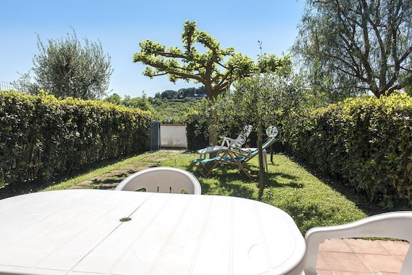 A patio area with a round table and chairs, surrounded by neatly trimmed hedges and trees.