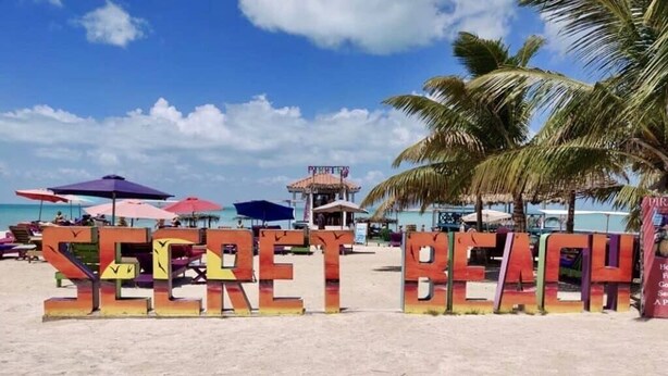 A beach with large, colorful letters spelling "SECRET BEACH" and palm trees in the background. - Mr. Ed's Adventures Belize (San Pedro)