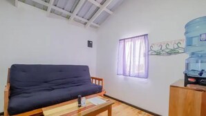A room with a wooden sofa, a small wooden table, a water dispenser, and a window with curtains. - Mr. Ed's Adventures Belize (San Pedro)