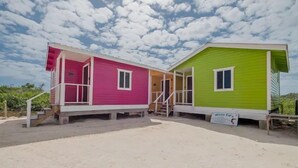 Two adjacent beach houses with a sandy ground and a clear sky. - Mr. Ed's Adventures Belize (San Pedro)
