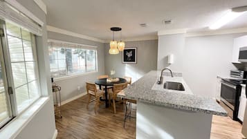 A modern kitchen with a granite countertop, a dining area with a round table and chairs, and a pendant light fixture.