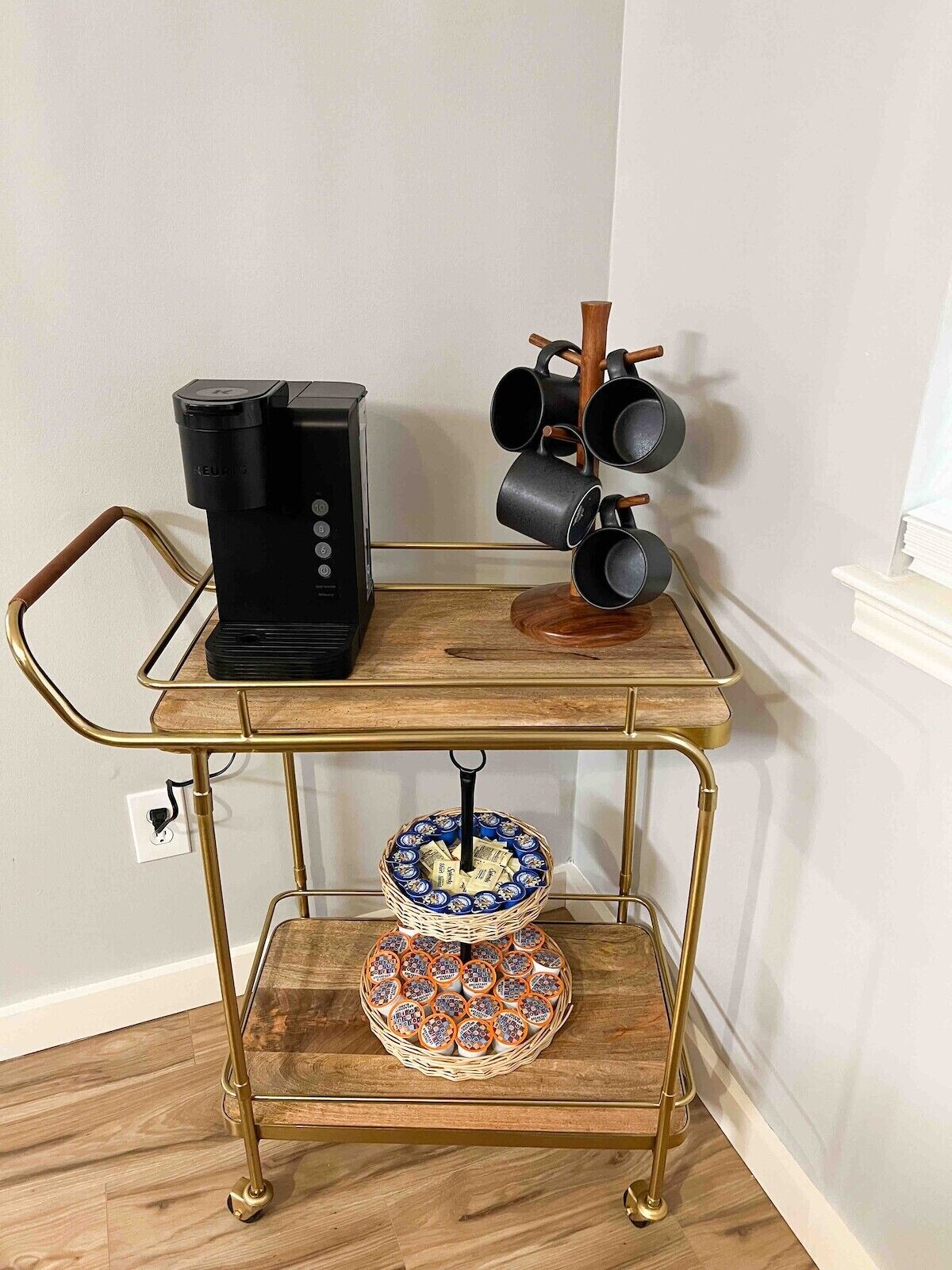Una estación de café con cafetera, portavasos y una cesta de cápsulas de café.