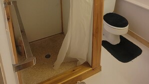 Un baño con ducha, inodoro y una ventana pequeña.