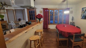 Un comedor con una mesa roja, sillas de madera y una encimera de cocina con taburetes.