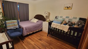 Un dormitorio acogedor con cama, cuna, silla, mesa y planta en maceta.