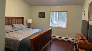A bedroom with a bed, a window with a view of trees, a bedside lamp, and a dresser. - Sasquatch Sanctuary (Crescent City)