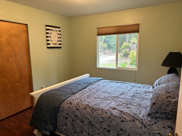 A bedroom with a bed, a window with a view of greenery, a door, and a wall with a decorative piece.