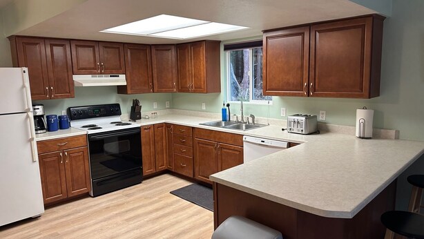 A modern kitchen with wooden cabinets, a built-in oven, a dishwasher, and a window with a view of trees. - Sasquatch Sanctuary (Crescent City)