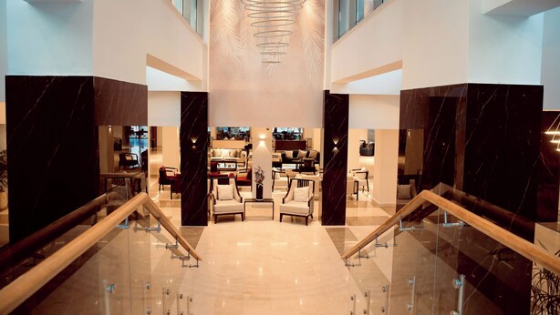 A spacious lobby with a central seating area, a modern chandelier, and a glass staircase. - Ocean Grand Hotel (Ramallah)