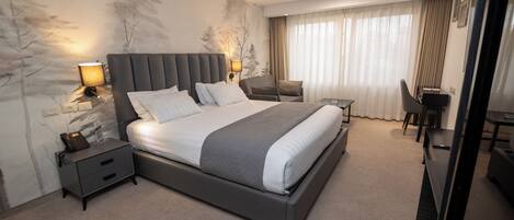 Una habitación de hotel moderna con una cama grande, mesitas de noche, un escritorio y una silla.