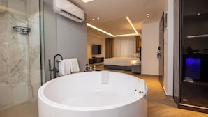 A modern hotel room with a large bathtub, a television, a bed, and a shower area. - Ocean Grand Hotel (Ramallah)