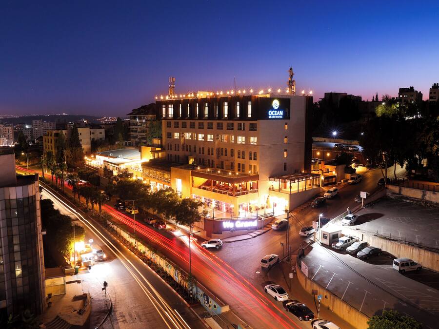 A multi-story hotel with a prominent 'Ocean Grand Hotel' sign, a parking area, and a street with light trails indicating traffic.