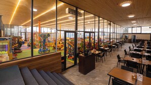A spacious indoor area with large windows, wooden ceiling, and a play area visible through the glass. - Ocean Grand Hotel (Ramallah)