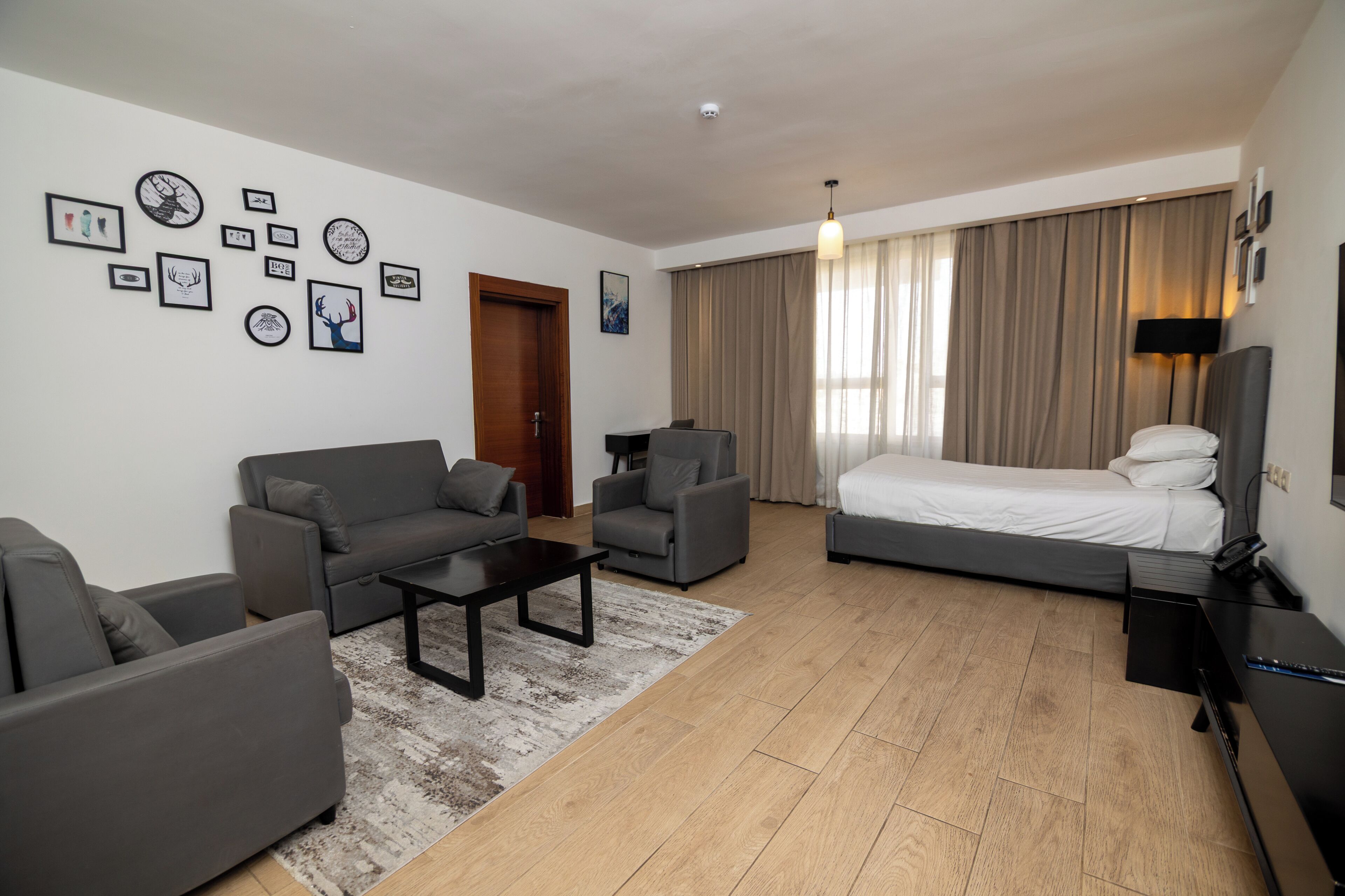 A modern hotel room with a sofa, armchair, bed, and a coffee table.