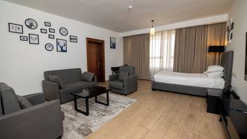 A modern hotel room with a sofa, armchair, bed, and a coffee table.