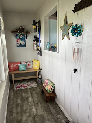 A cozy room with a wooden bench, a small stool, a welcome mat, and decorative items like a star and a flower-shaped wind chime.