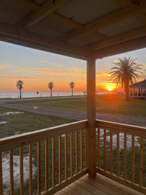 Eine Holzterrasse mit Blick auf den Sonnenuntergang über dem Meer, Palmen und einem Steg.