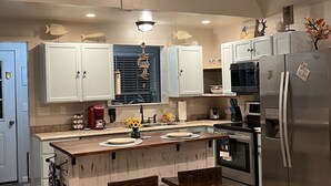 Une cuisine avec un îlot central, des tabourets en bois, un réfrigérateur et un four à micro-ondes.