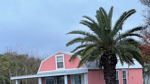 Une maison rose avec un porche blanc et un palmier devant.