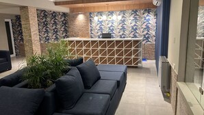 A modern living area with a dark blue sofa, a decorative wall with leaf patterns, and a wooden reception desk.
