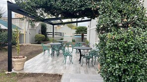 Une terrasse extérieure avec des chaises et des tables en métal vert, une pergola et un pot de fleurs.
