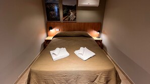 A hotel room with a large bed, two wall-mounted air conditioners, and two wall-mounted lamps.