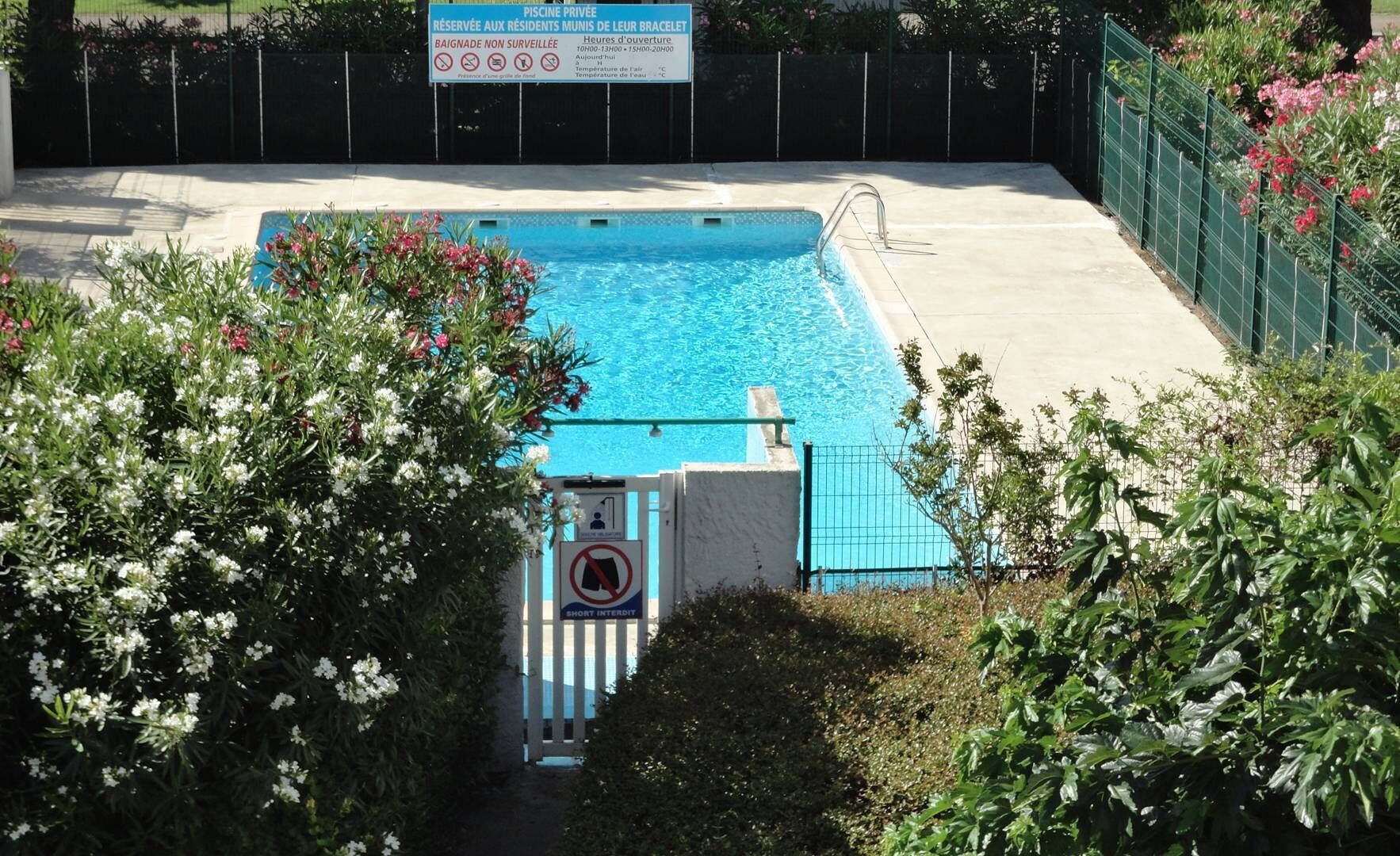 Une piscine privée, avec un panneau indiquant qu’elle est réservée aux résidents munis d’un bracelet, et un panneau à l’entrée indiquant qu’il est interdit d’y porter des shorts.