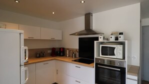 Een kleine keuken met witte kastjes, een magnetron, een oven en een koffiezetapparaat.