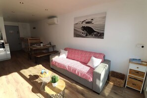 Ein Wohnzimmer mit einer Couch, einem Esstisch, einem kleinen runden Tisch mit Pflanze und einer Wand-Klimaanlage.