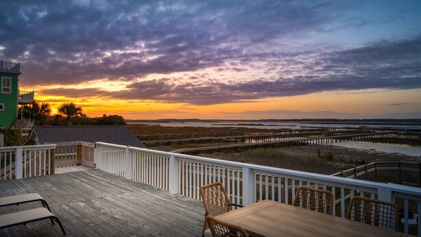 A wooden deck with a table and chairs, overlooking a sunset over a marshy landscape. - Swim Spa with River Views - Pet friendly, Private Dock, Marsh Views - On Beach Time (Folly Beach)