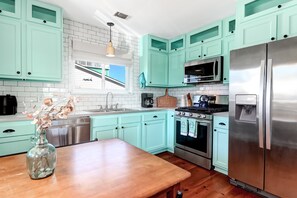 A kitchen with teal cabinets, stainless steel appliances, a wooden table, and a vase with dried flowers.