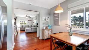A modern kitchen with wooden flooring, a dining table with chairs, a pendant light, and a view of the outdoors through a large window. - Swim Spa with River Views - Pet friendly, Private Dock, Marsh Views - On Beach Time (Folly Beach)