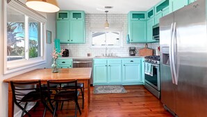 A kitchen with teal cabinets, a wooden dining table, and a stainless steel refrigerator. - Swim Spa with River Views - Pet friendly, Private Dock, Marsh Views - On Beach Time (Folly Beach)