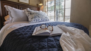 A neatly made bed with a quilted cover, a pair of glasses, and an open book on it. - The Franklin Castle (Tahlequah)