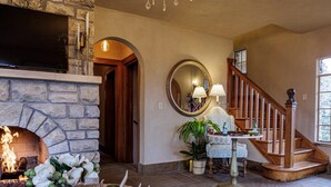 A cozy living room with a stone fireplace, a chandelier, a comfortable sofa, and a staircase leading to another level. - The Franklin Castle (Tahlequah)