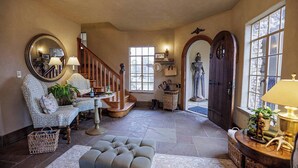 A spacious living room with a wooden staircase, a large mirror, and a statue. - The Franklin Castle (Tahlequah)