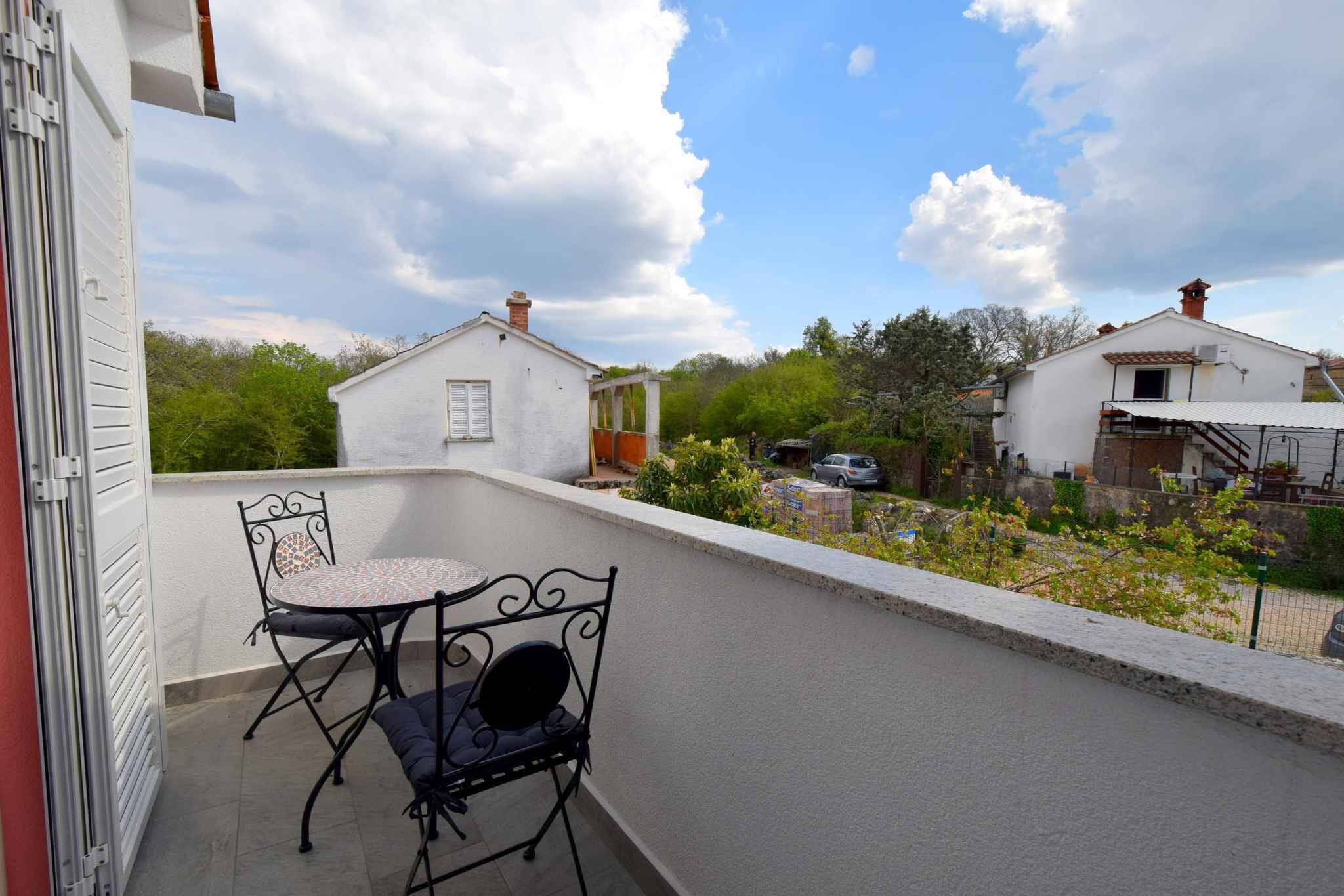 A balcony with a table and two chairs, a white building in the background, and a clear sky.