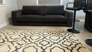 Een moderne woonkamer met een donkerbruine bank, een getextureerd vloerkleed en een zwarte barkruk.