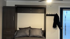 Een slaapkamer met een bed, een donker houten garderobe, een plafondventilator en een deur met uitzicht.