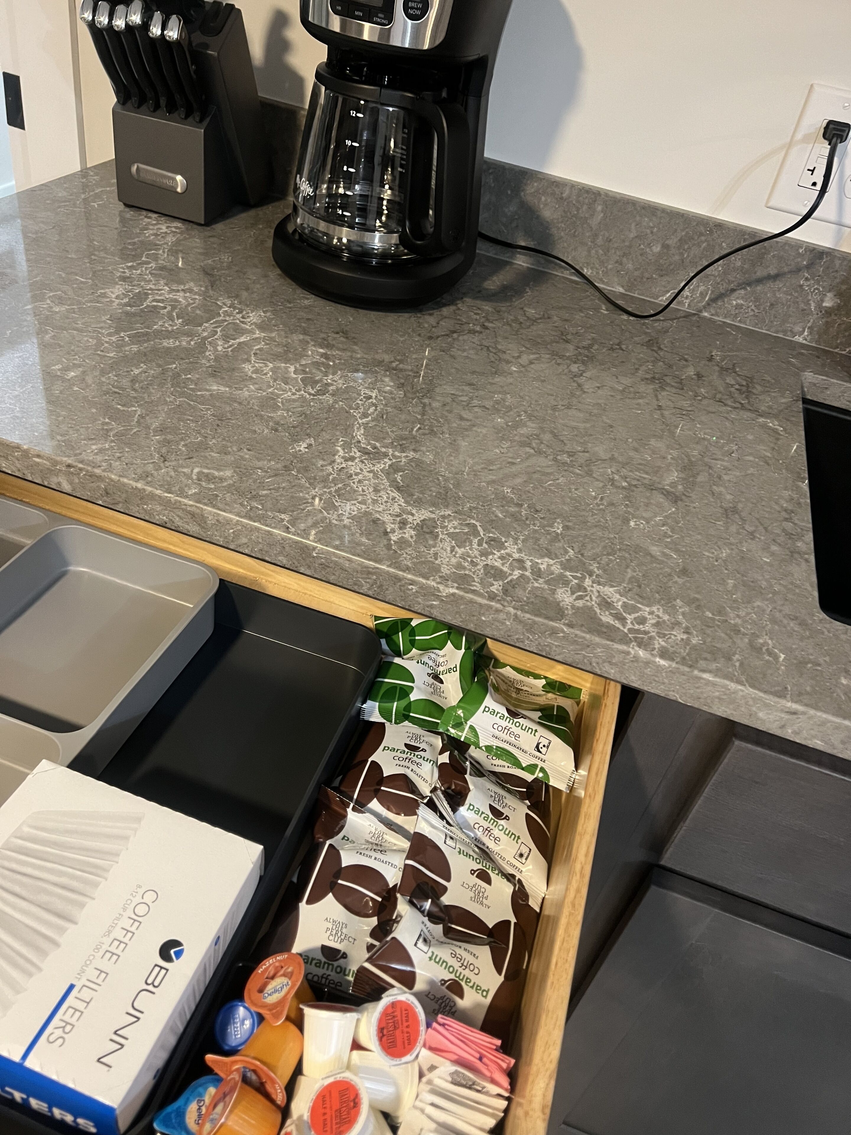 Eine Küchenarbeitsplatte mit Kaffeemaschine, einem Messerblock und einer Schublade mit Kaffeekapseln und einer Packung Kaffeefiltern.