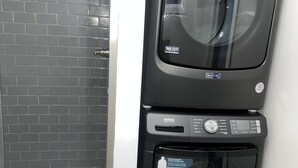 Een gestapelde wasmachine en droger met een sticker voor 10 jaar garantie, in een badkamer met een betegelde douche.