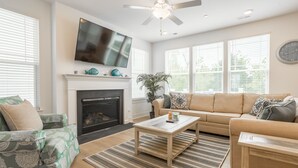 A living room with a fireplace, a television mounted above it, a sofa, a coffee table, and a large window with blinds. - Recently Built  Rehoboth Beach Townhouse Pool Parking Sleeps 16 (Rehoboth Beach)