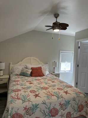 A bedroom with a bed, a ceiling fan, a nightstand, and a window. - Sea Turtle Getaway (Ventnor City)