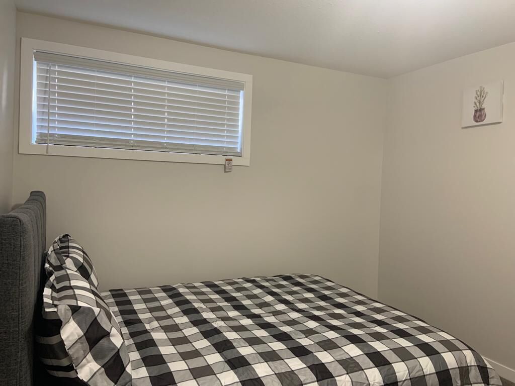 A small, single-bed room with a checkered bedspread, a window with blinds, and a small wall-mounted picture.