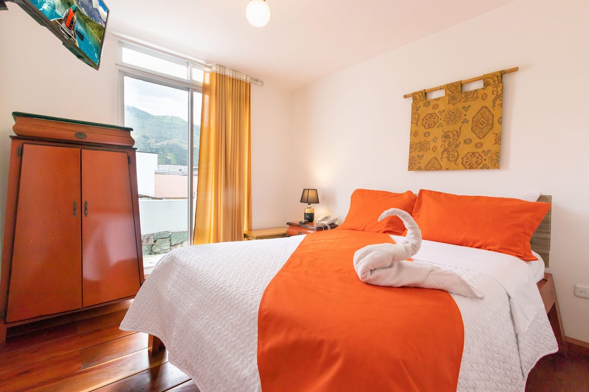 Une chambre d’hôtel avec un lit, une armoire en bois, une table de chevet avec une lampe et une fenêtre avec des rideaux.