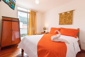 A hotel room with a bed, a wooden wardrobe, a nightstand with a lamp, and a window with curtains.
