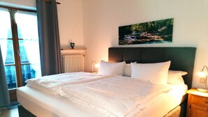 Un lit bien fait, avec du linge de lit blanc, une tête de lit et une table de chevet sur laquelle se trouve une lampe.