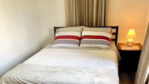 Siististi pedattu sänky, jossa on raidallisia tyynyjä, yöpöydällä oleva lamppu ja puulattia.